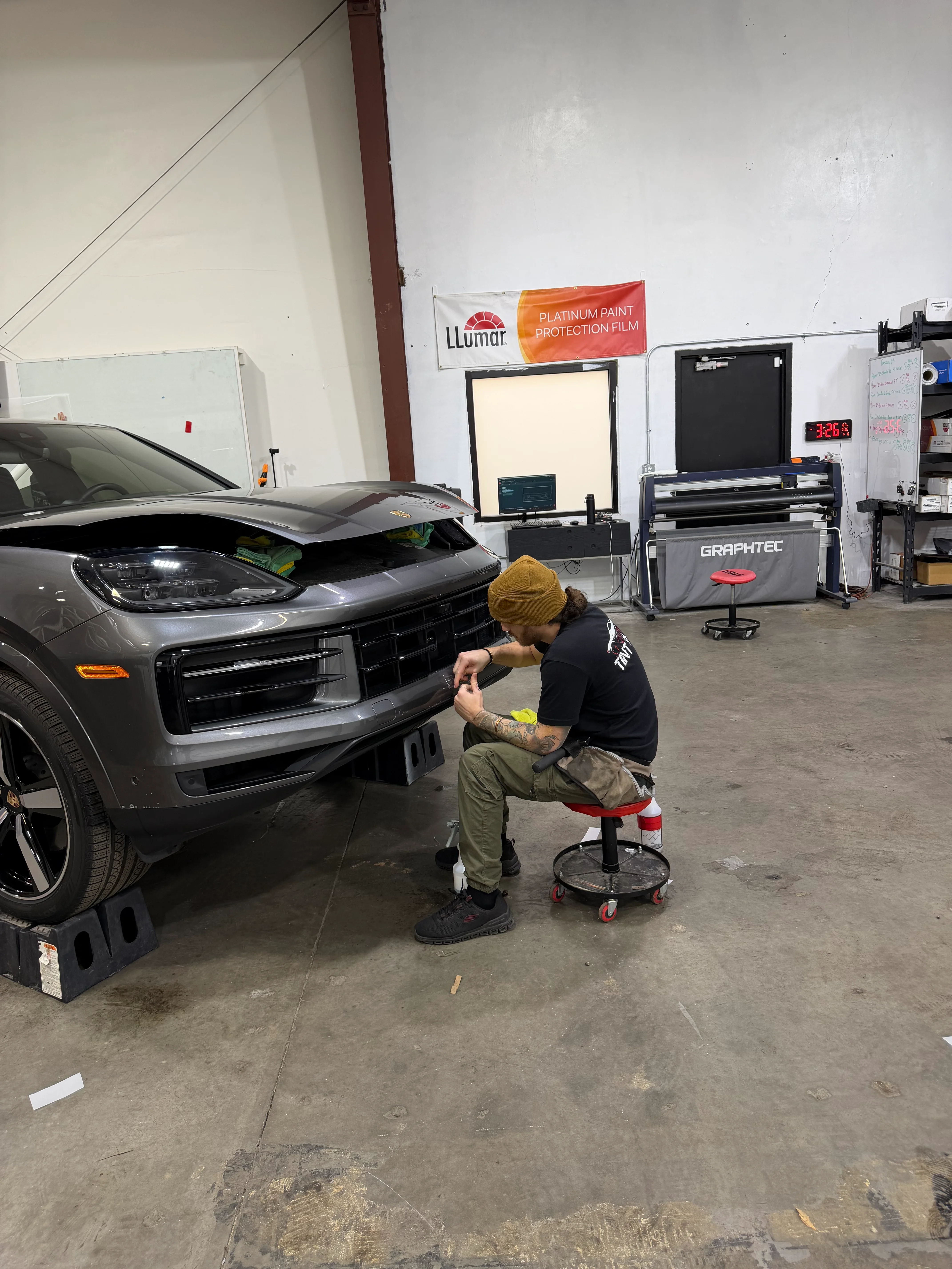 Professional installer applying paint protection film to the front bumper of a gray Porsche Cayenne SUV in St. George, Southern Utah.