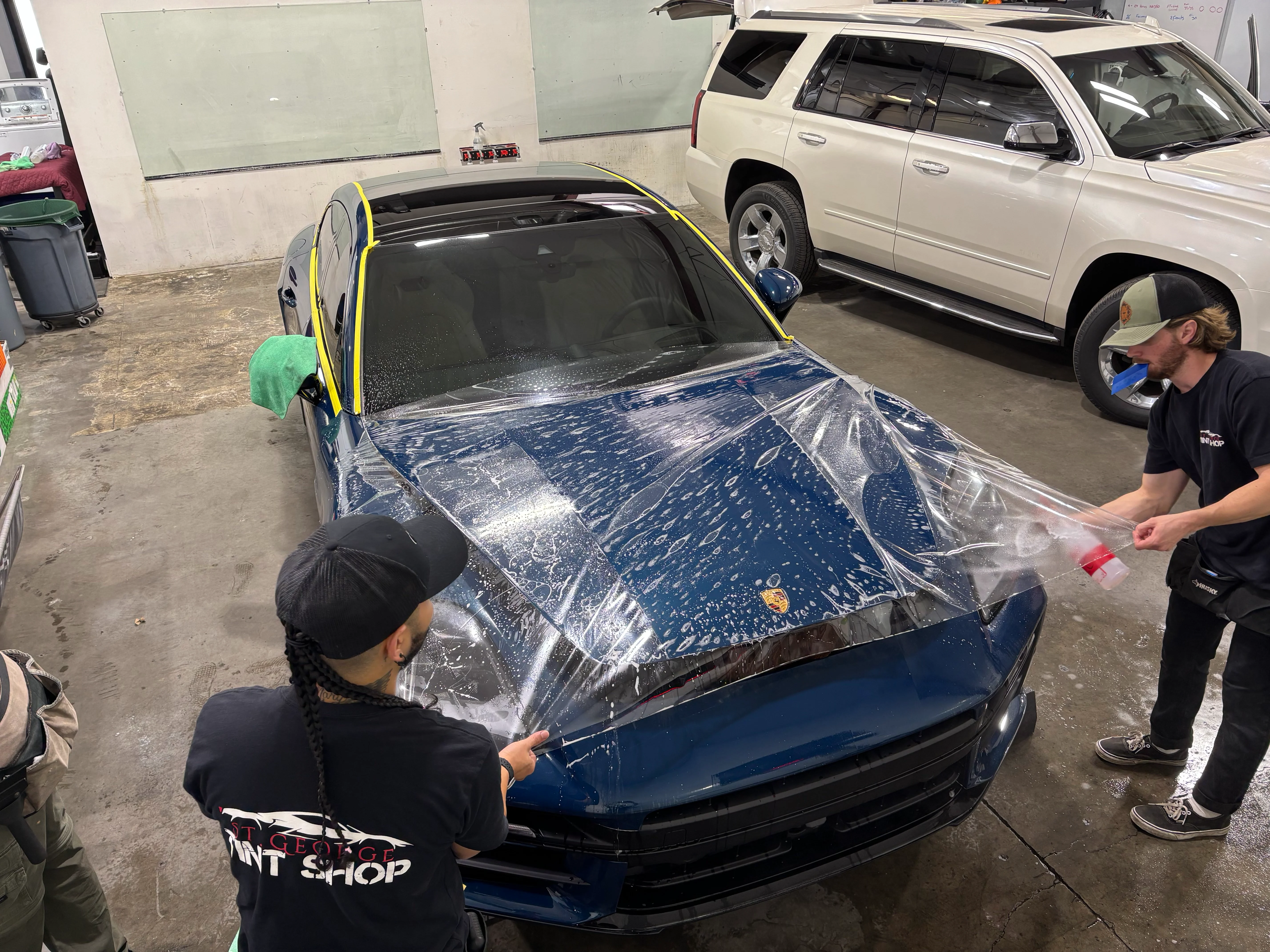 Technicians apply clear paint protection film (PPF) to a blue Porsche sedan, ensuring precise fit in St. George, Southern Utah.