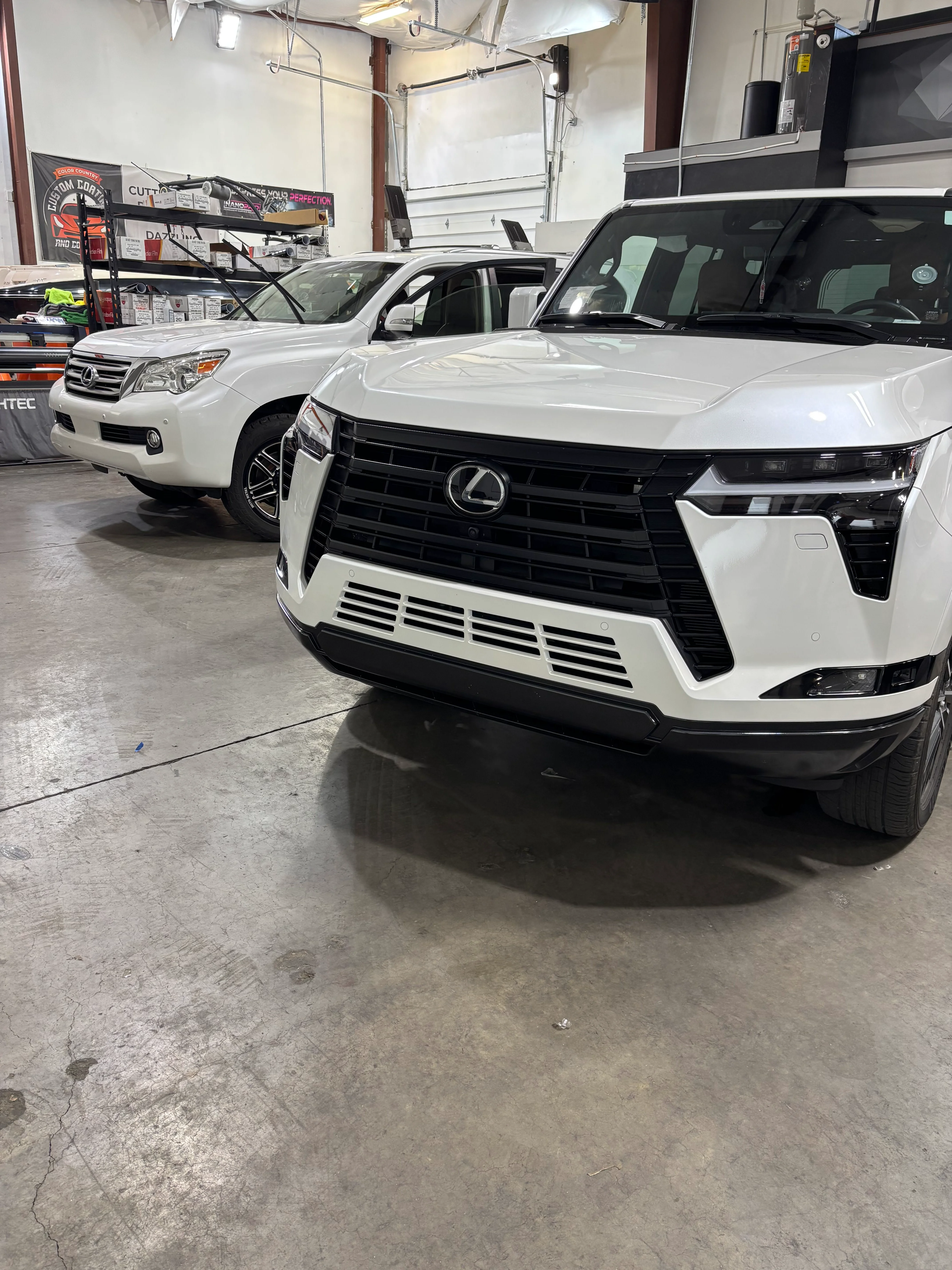 Two pristine white Lexus SUVs, a GX and a newer LX model, inside a professional tint and PPF shop in St. George, Utah.