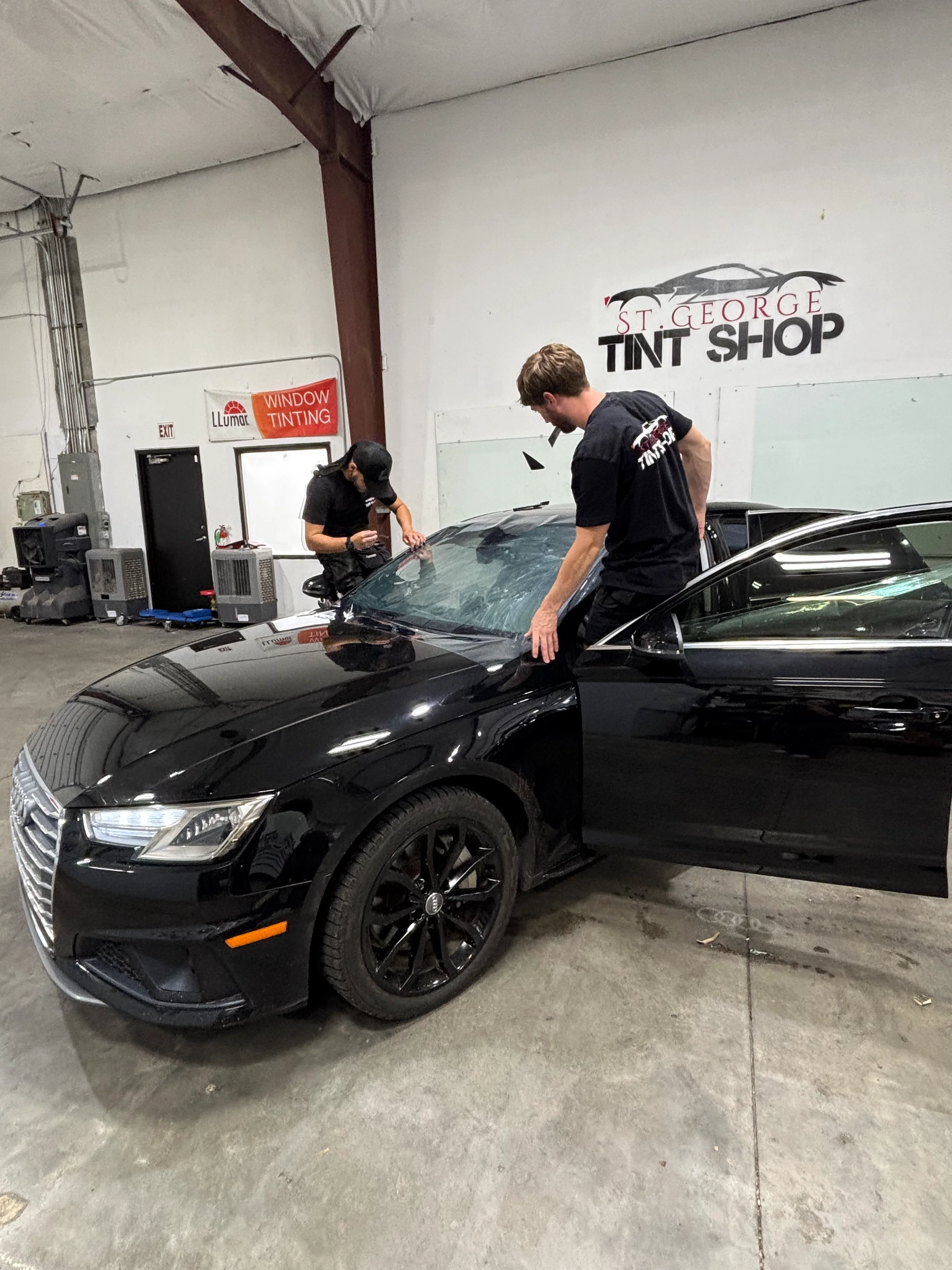 Professional technicians applying ceramic window tint to a black Audi sedan at a tint shop in St. George, Southern Utah.