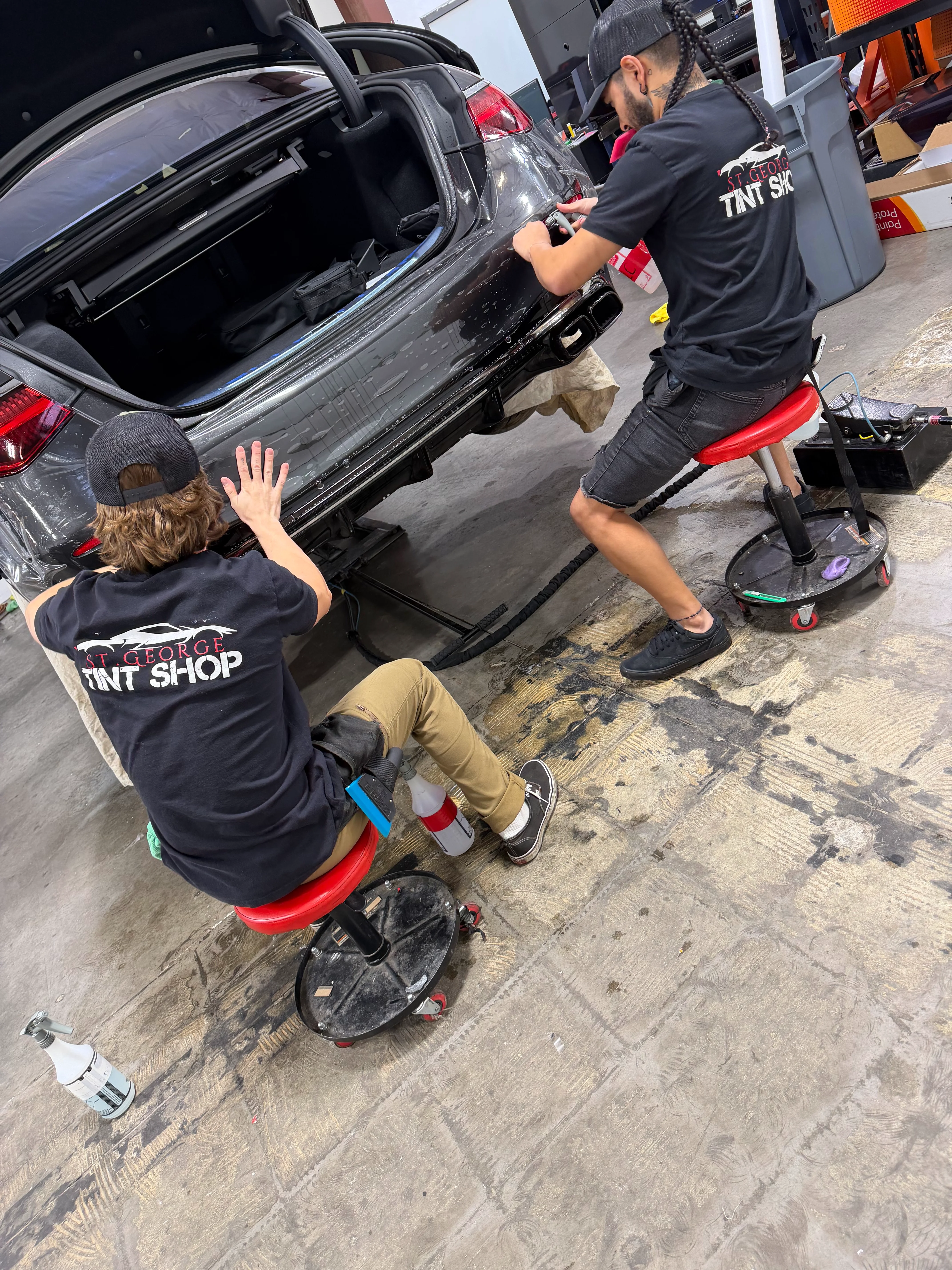 Two technicians apply Paint Protection Film to the rear bumper of a dark sedan at a professional tint shop in St. George, Southern Utah.