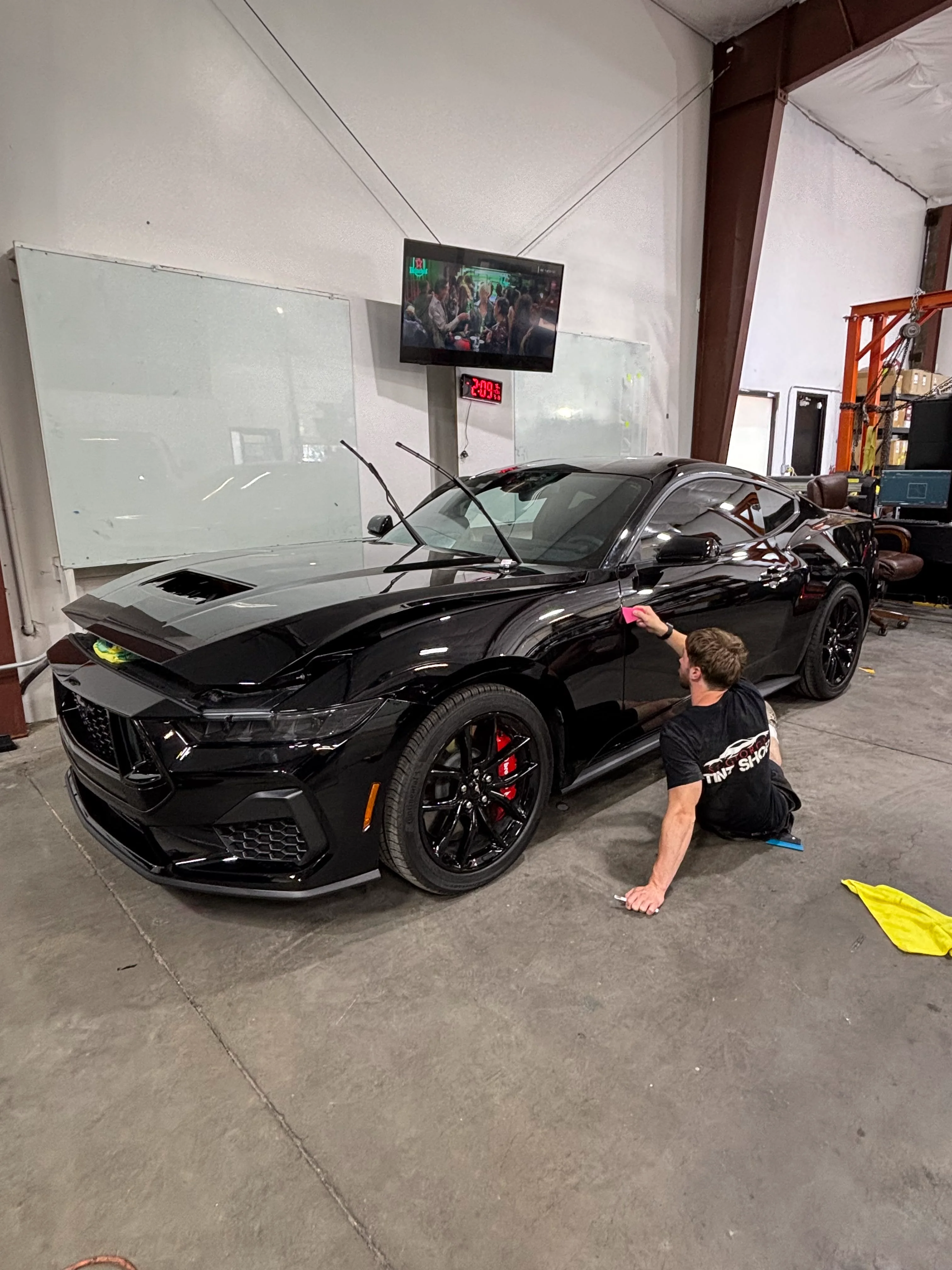 Professional installer applying ceramic window tint to a sleek black Ford Mustang in a St. George tint shop, ensuring privacy and UV protection for this sports coupe.