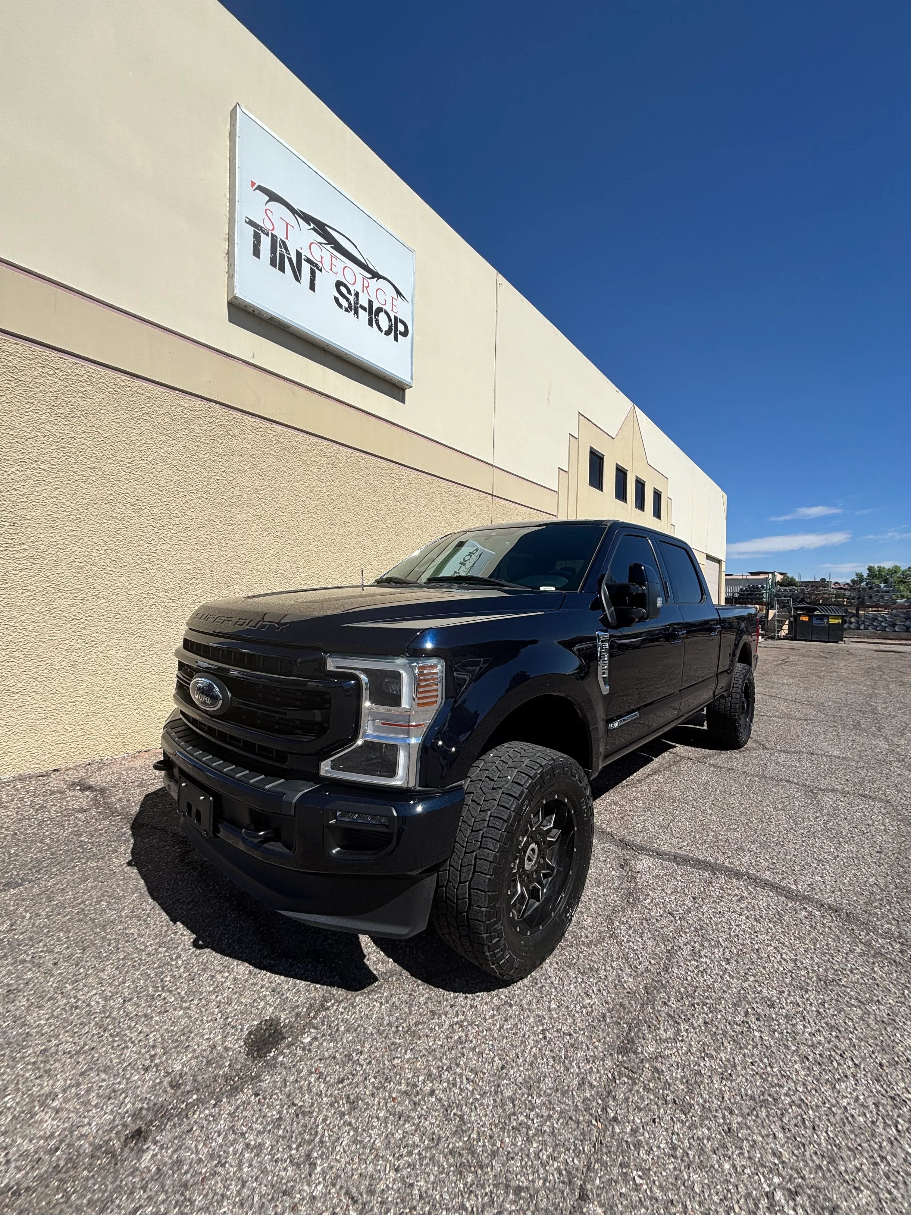 Dark blue Ford Super Duty truck with new ceramic window tint parked in front of St. George Tint Shop in Southern Utah.