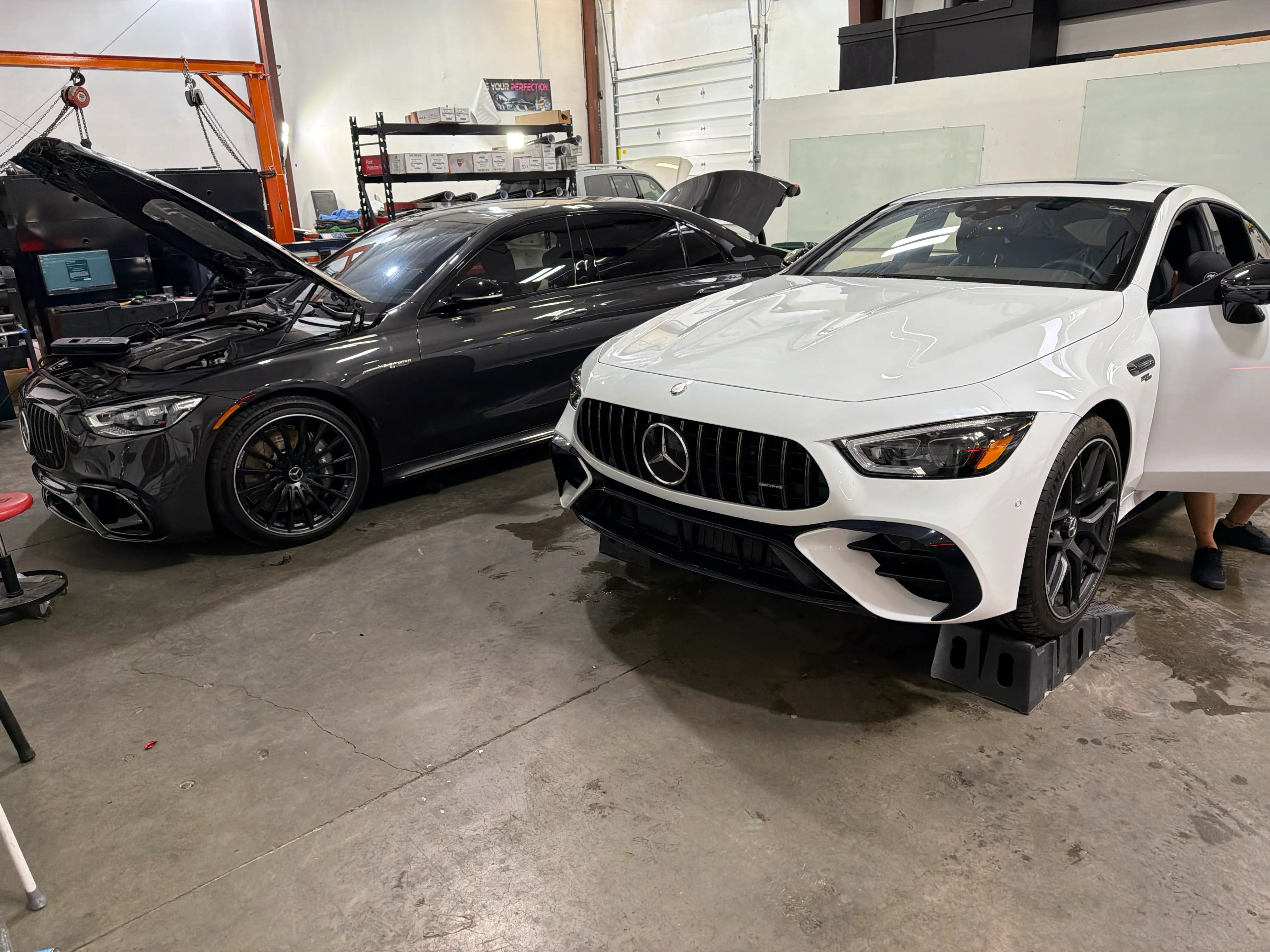 Two Mercedes-AMG sedans, one black and one white, being prepared for professional tint or PPF service in a St. George film shop.