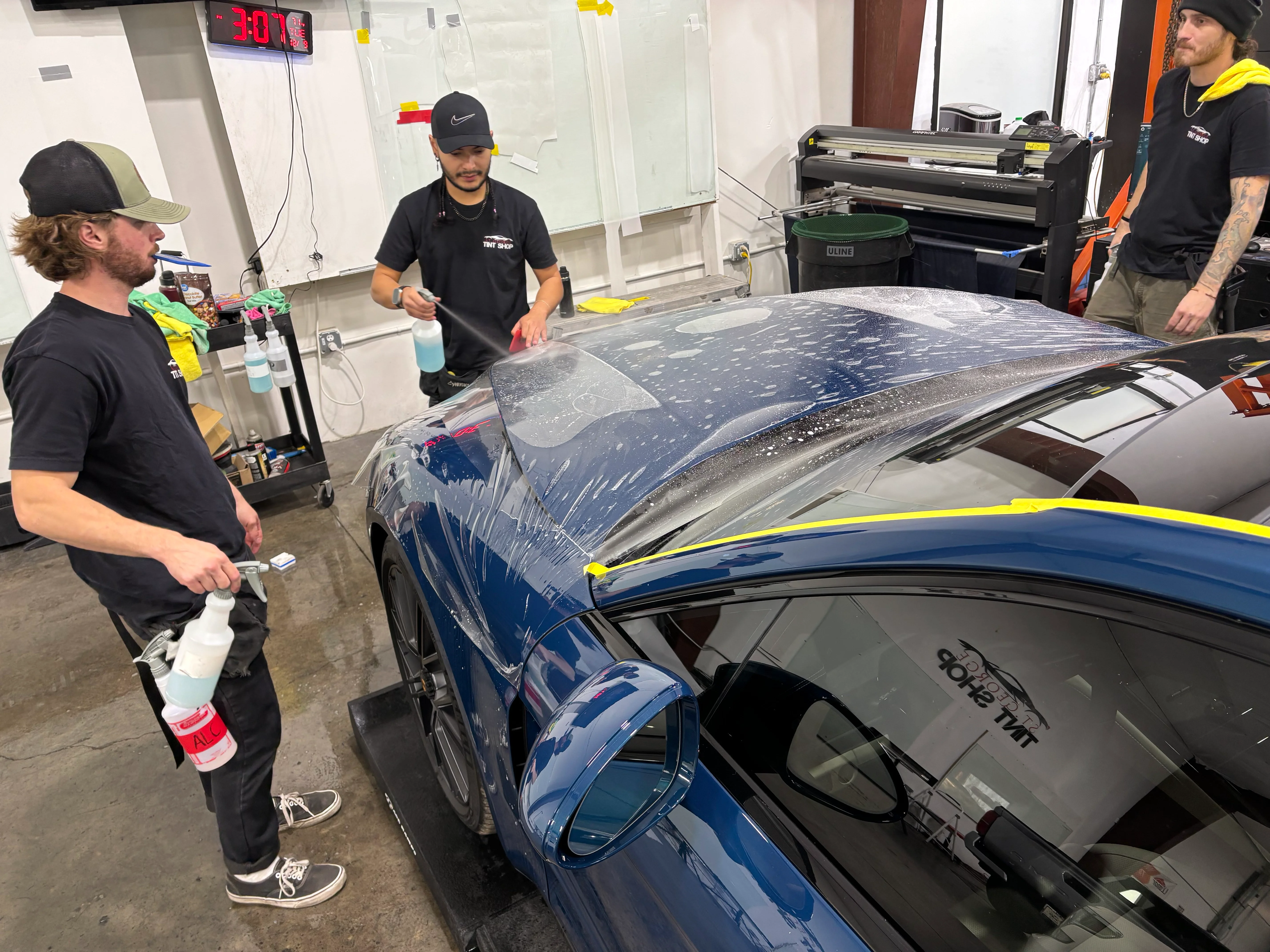 Professional technicians applying paint protection film (PPF) to the hood of a blue luxury sedan in St. George, Southern Utah.
