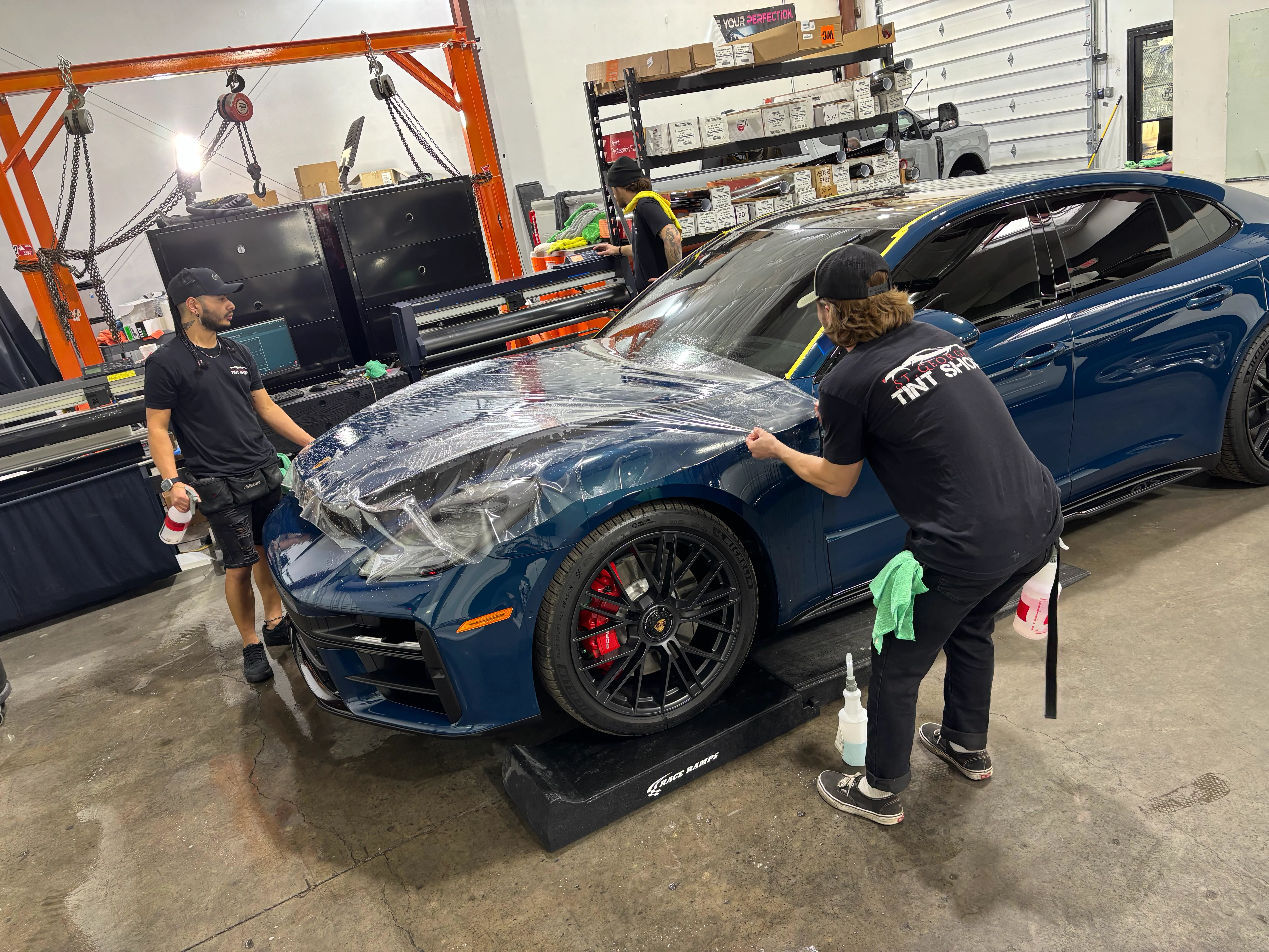 Team applying clear paint protection film to the front of a blue Porsche Panamera sedan in our St. George shop.