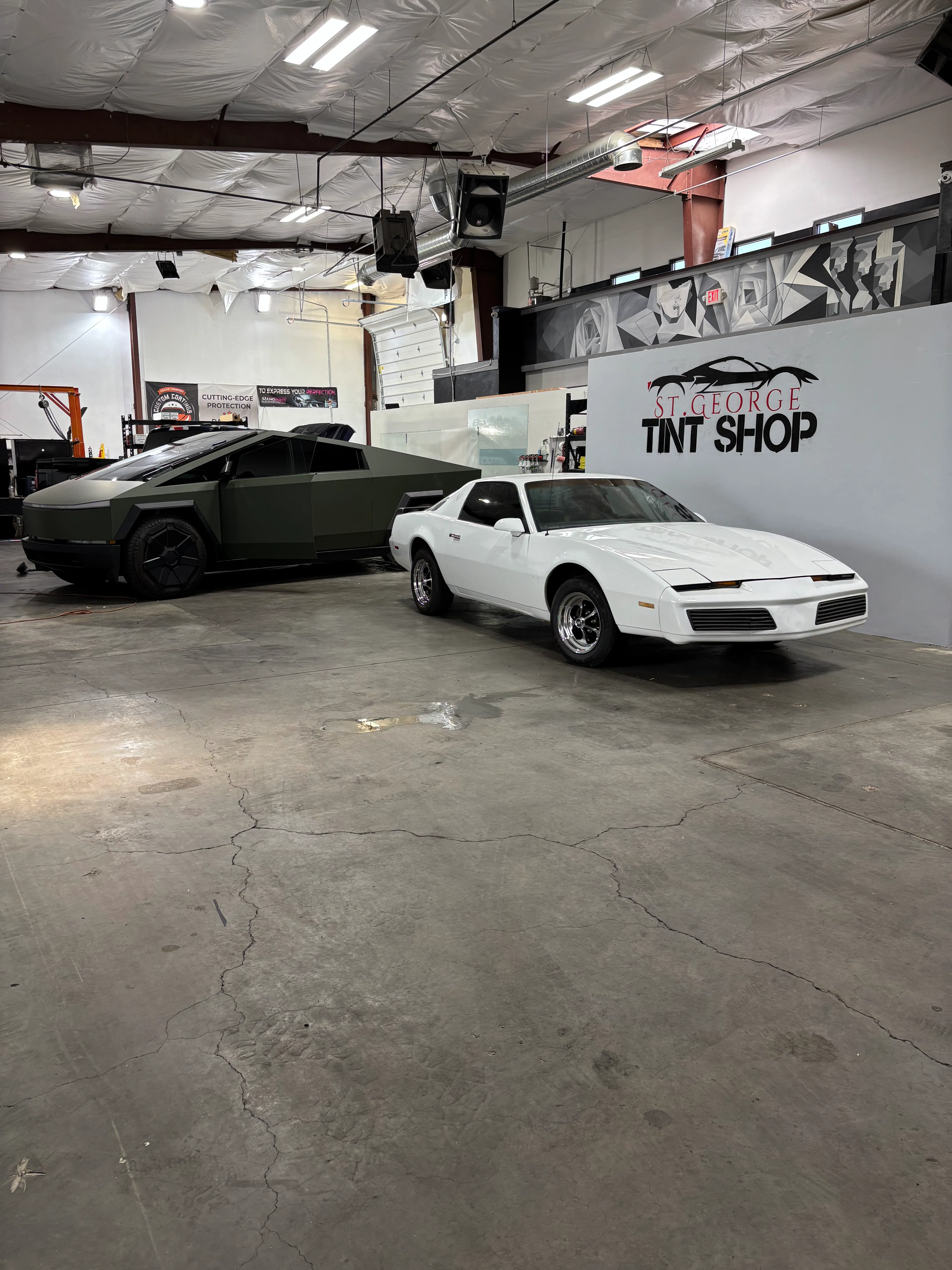 A Tesla Cybertruck and white Pontiac Firebird with professional window tinting in a St. George, Utah tint shop. Features a Cybertruck wrapped in matte green.